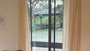 A room with two wicker chairs, a small table, and a view of an outdoor area with a gazebo and picnic table.
