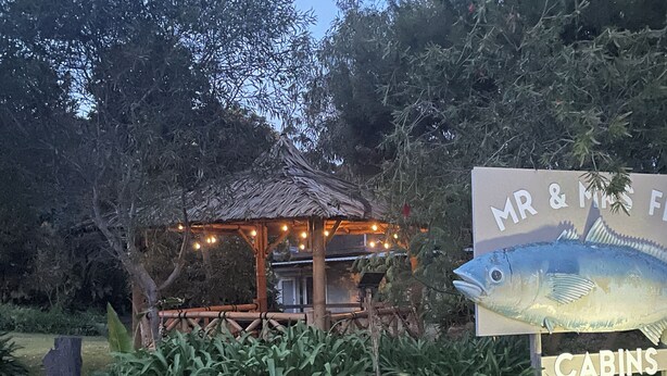 A wooden gazebo with string lights, surrounded by lush greenery and a sign for 'Mr & Mrs Fish Cabins'.
