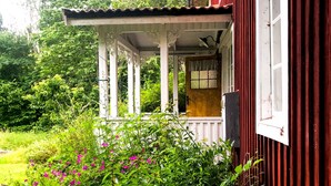Una casa de madera con porche, rodeada de exuberante follaje y plantas en flor.