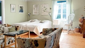 Un dormitorio con cama doble, una mesita de noche de madera, un sillón floral, una silla de mimbre y un aparador con cestas.