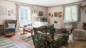Una habitación acogedora con suelo de madera, un sofá floral, una mesa de madera y una silla blanca.