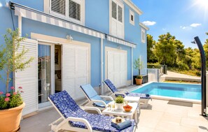 A poolside area with lounge chairs, a small table with a plant, and a clear blue pool. - 3 bedroom beautiful home in Sutivan (Sutivan)