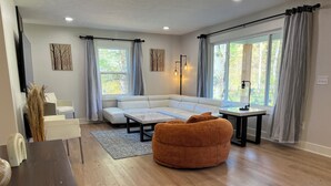 A modern living room with a sectional sofa, a coffee table, and a bean bag chair. There is a dining table with chairs, a lamp, and artwork on the walls. - Huge home w/ 4 king beds and a huger yard. On Grand River on 11 acres (Ada)