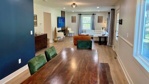 A spacious living room with a large wooden dining table, comfortable seating, a flat-screen TV, and a large window providing natural light. - Huge home w/ 4 king beds and a huger yard. On Grand River on 11 acres (Ada)