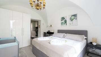 A modern bedroom with a large bed, a desk, and a kitchenette in the background.