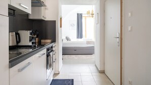A narrow hallway leading to a bedroom with a bed, a window with curtains, and a kitchen area with a coffee maker and utensils. - COY Apartments Wachau - Relaxation In Style (Mautern an der Donau)