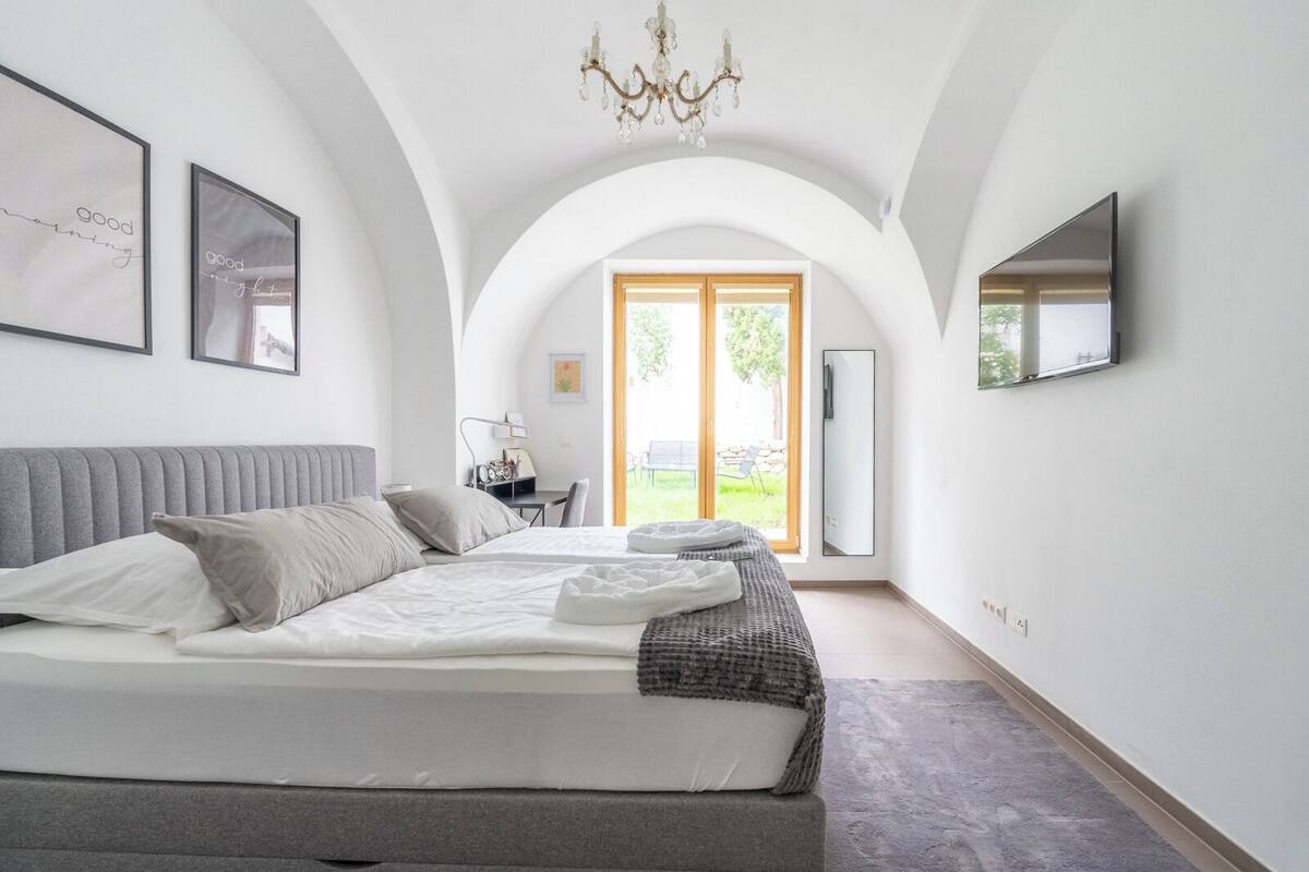 Ein modernes Schlafzimmer mit einem großen Bett, einem Schreibtisch und Blick ins Freie durch ein großes Fenster.
