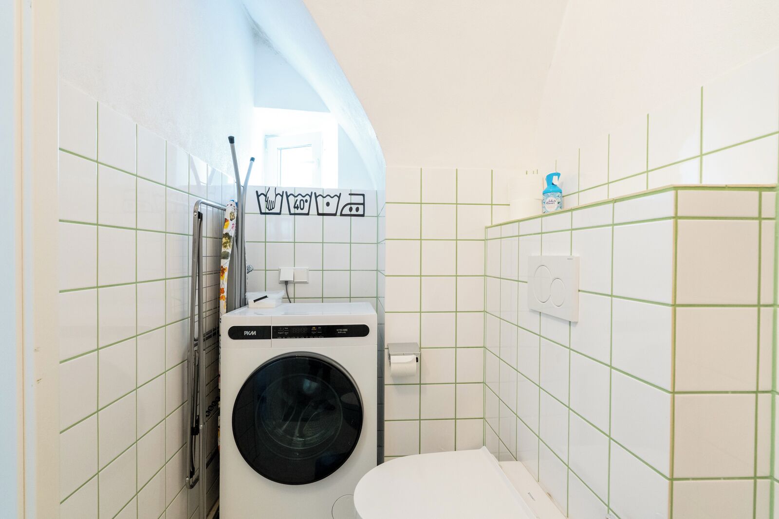 Una lavanderia funzionale con lavatrice a carica frontale, un WC e un piccolo lavandino.