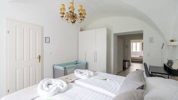 Een hotelkamer met twee bedden, een bureau, een stoel, een kroonluchter en uitzicht op de gang.