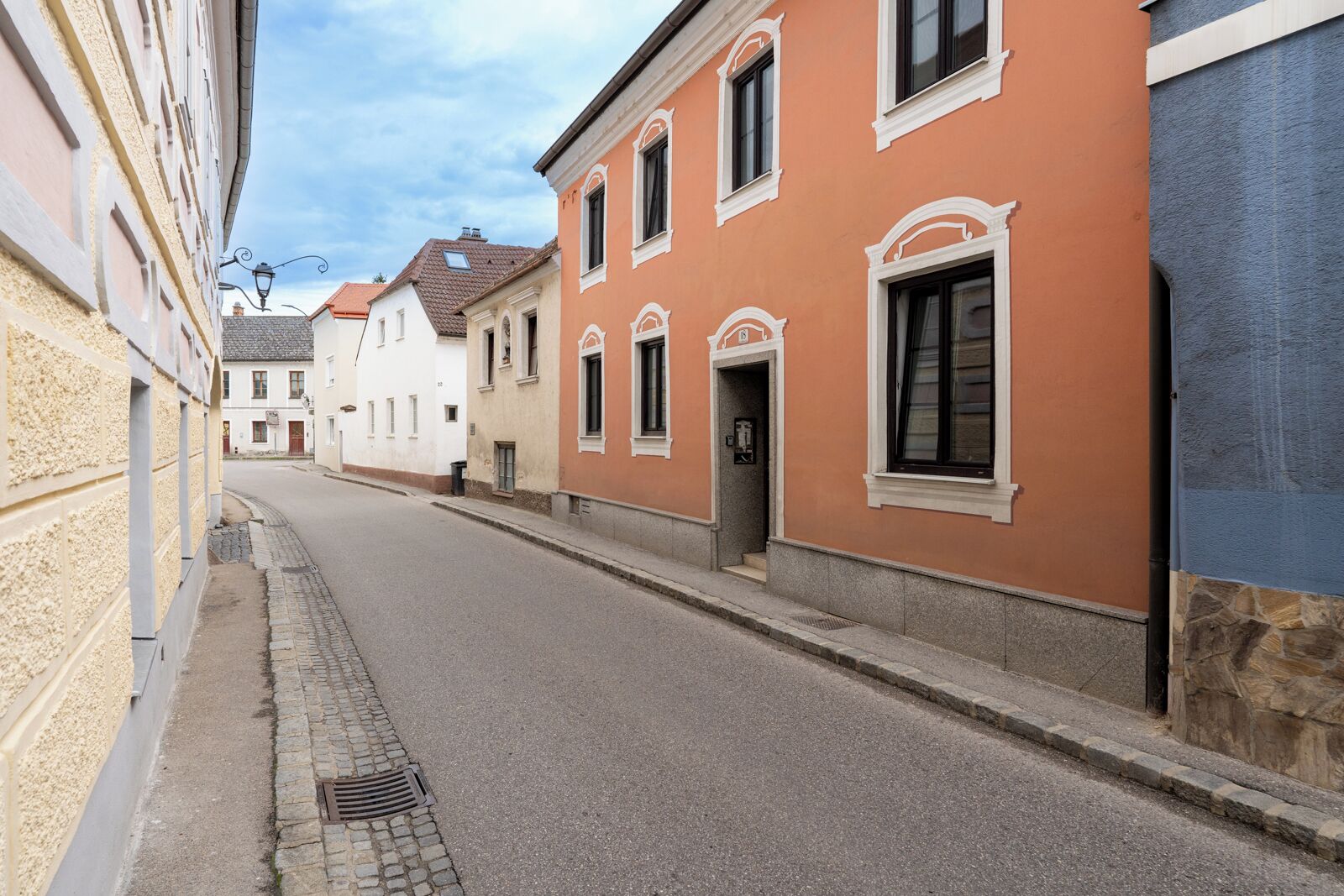 A narrow street lined with buildings featuring classic architecture and a cobblestone sidewalk.