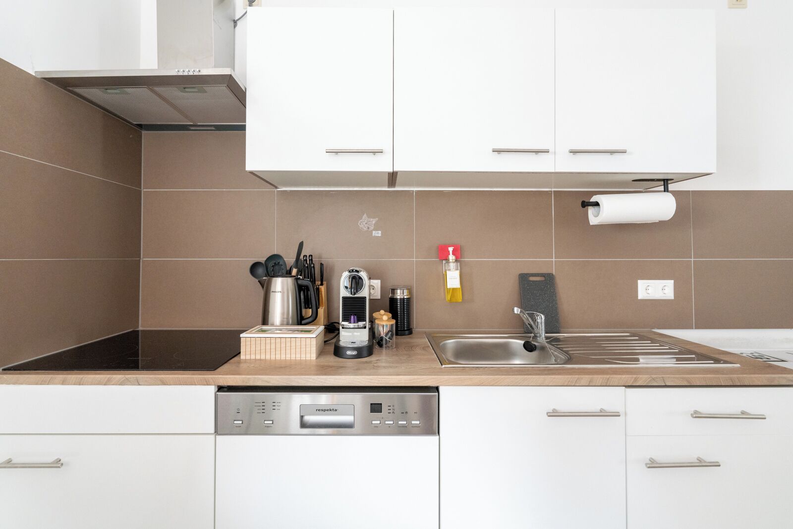 Una cucina moderna con mobili bianchi, un lavello in acciaio inossidabile, una macchina da caffè e una lavastoviglie.
