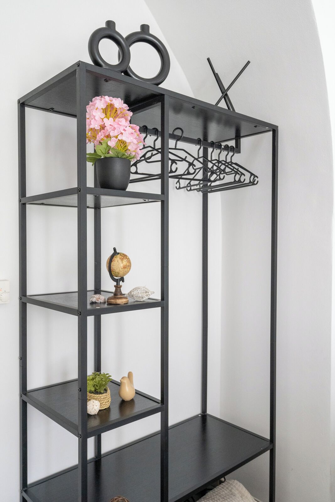 A black metal shelf unit with a globe, a potted plant, and a vase of flowers.