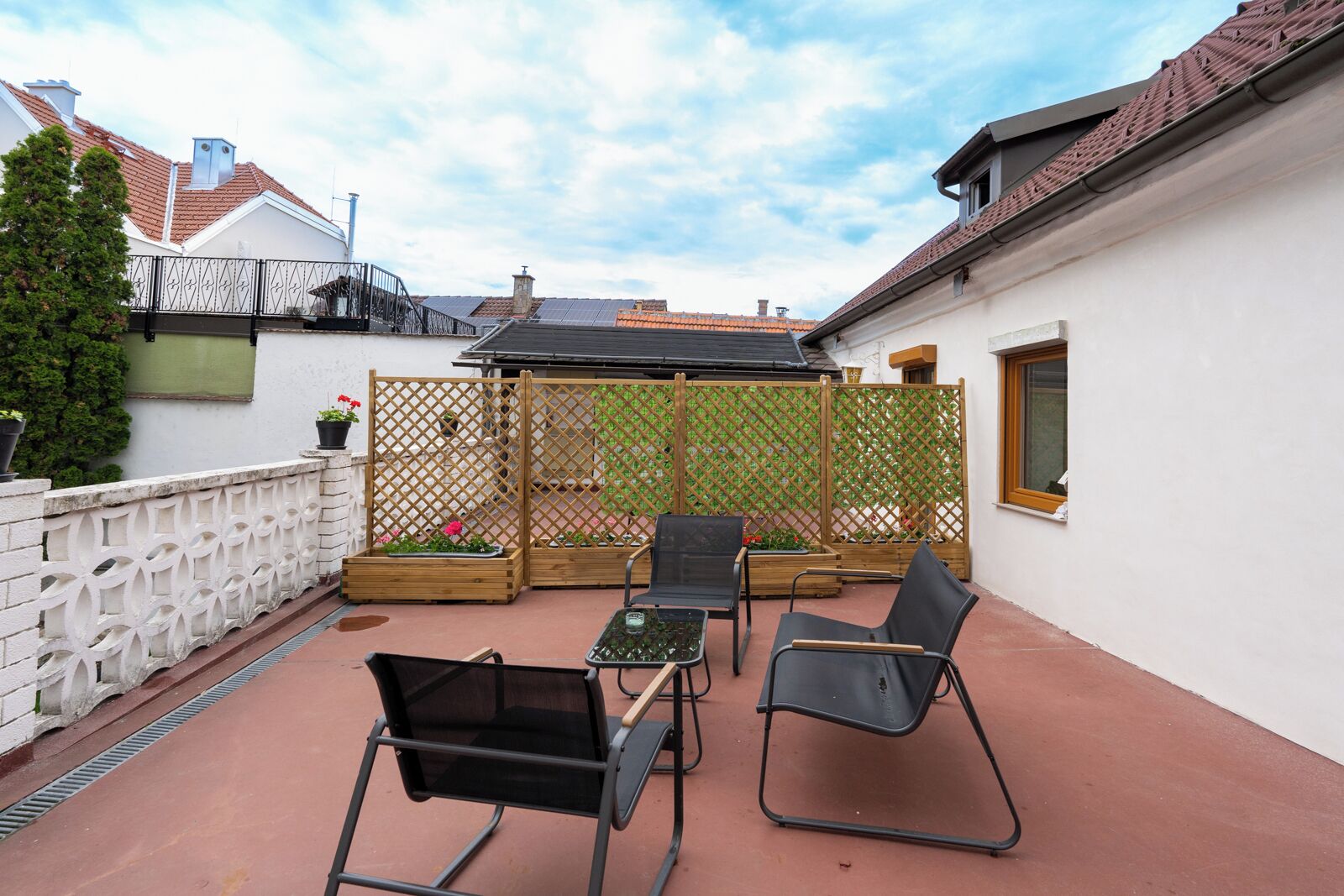 An outdoor patio area with a white wall, a wooden fence, and a metal table with two chairs.