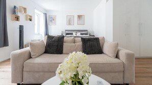 A modern living room with a beige sofa, a coffee table with a white vase, and a bed in the background. - COY Apartments Wachau - Relaxation In Style (Mautern an der Donau)