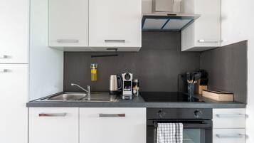 A modern kitchen with white cabinets, a black countertop, a stainless steel sink, a coffee machine, and a range hood.