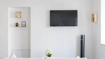 Uma sala de estar moderna com televisão de tela plana na parede, um sofá, uma mesinha com planta em vaso e um aquecedor portátil.