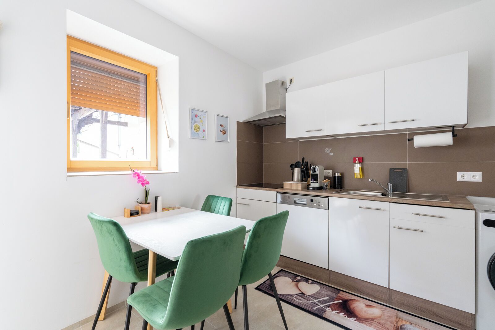 A compact kitchen with white cabinets, a built-in oven, and a window with blinds.