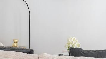 Un soggiorno moderno con una TV a schermo piatto montata al muro, un divano, un tavolino con una lampada e una piccola mensola con oggetti decorativi.