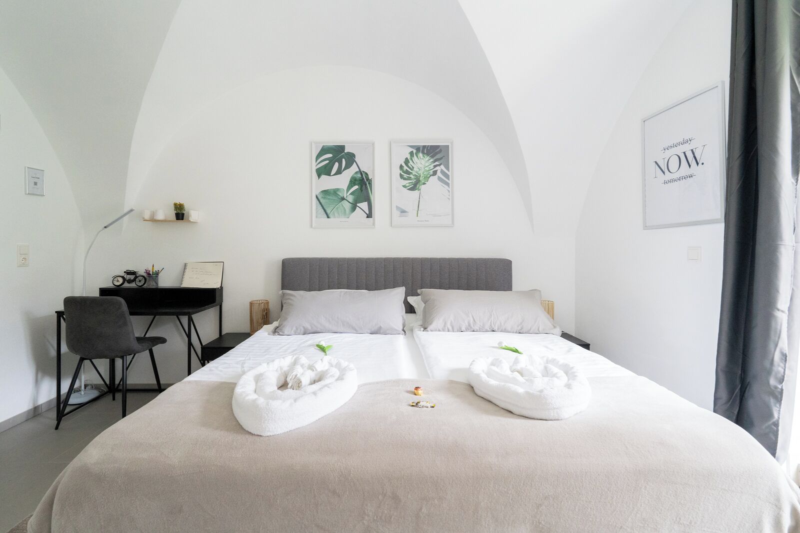 Ein Schlafzimmer mit einem großen Bett, zwei Kissen, einem Schreibtisch mit Stuhl und Bildern an den Wänden.