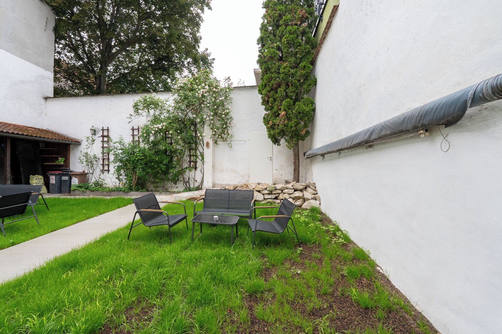 Un patio con mesa y sillas, rodeado por un muro blanco y follaje.