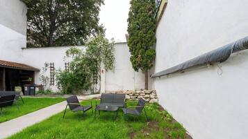 Un patio con mesa y sillas, rodeado por un muro blanco y follaje.