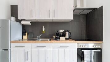 A modern kitchen with light wood cabinets, a stainless steel refrigerator, a coffee maker, and a kettle on the counter.