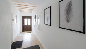 A hallway with framed artwork on the walls, a wooden door at the end, and a tiled floor. - COY Apartments Wachau - Relaxation In Style (Mautern an der Donau)