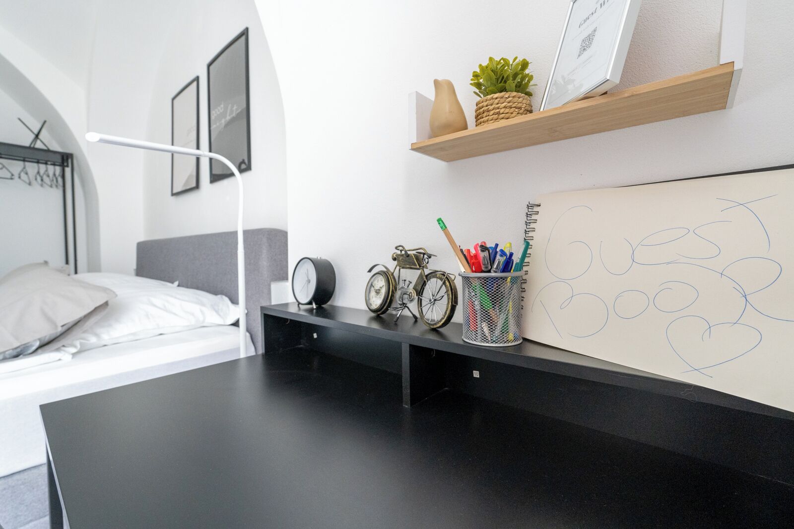 Un dormitorio moderno con cama, escritorio con bicicleta, estante con planta y pared con dibujo.