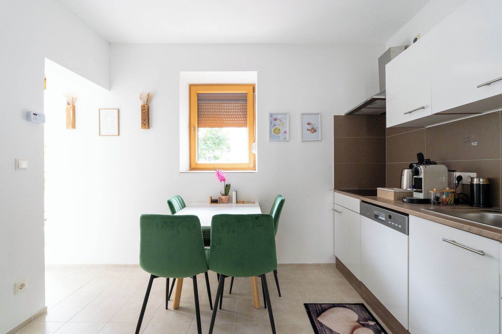 Cocina compacta con zona de comedor, que incluye ventanal, armarios blancos y una cafetera.