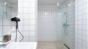 A bathroom with white tiled walls, a shower, a hairdryer, and a sink.