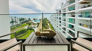 En balkong med en hängmatta, med utsikt över ett hotellkomplex med flera våningar, en pool och havet.