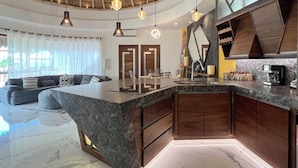 Una cocina moderna con una isla central, armarios de madera y un techo curvo con lámparas colgantes.