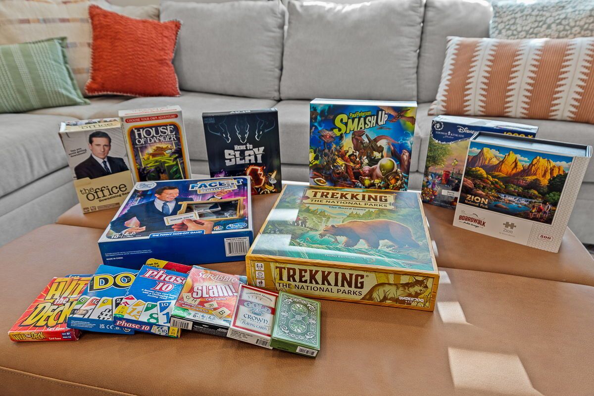 A variety of board games and card games on a coffee table in a living room.