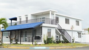 A two-story building with a blue roof, a balcony with black railings, and a staircase leading to the upper floor.