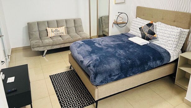 A bedroom with a bed, a grey sofa, a small table, and a mirror.