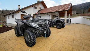 Two ATVs parked in front of a house with a tiled roof and a garden.