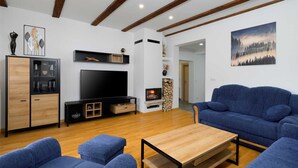 A modern living room with a flat-screen TV, a fireplace, blue sofas, and wooden flooring.