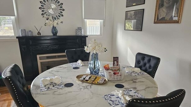 Un coin repas comprenant une table ronde en marbre, des chaises à revêtement noir, un vase avec des fleurs et un élément décoratif mural.