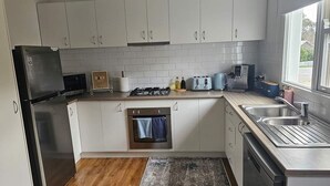 Une cuisine moderne avec des armoires blanches, un réfrigérateur en acier inoxydable, un four encastré, une cuisinière à gaz, une machine à café et un évier.