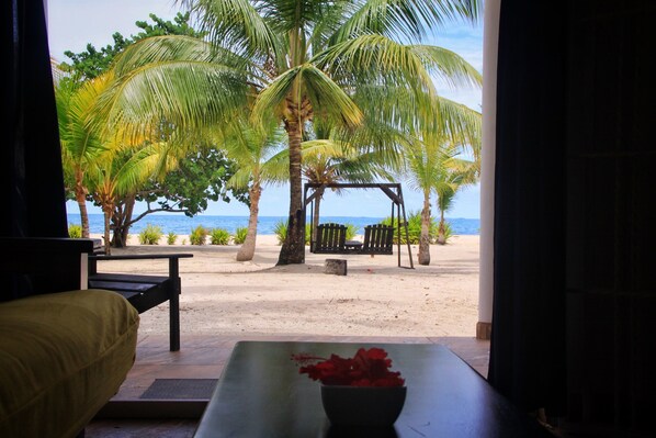 A beach view with a wooden swing set, palm trees, and a sandy beach.