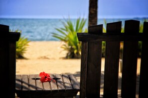 A wooden bench with a red flower on it, overlooking a sandy beach with palm trees and the ocean in the background. - Cozy Beachfront Suite for Couples, Ground Floor (Placencia)