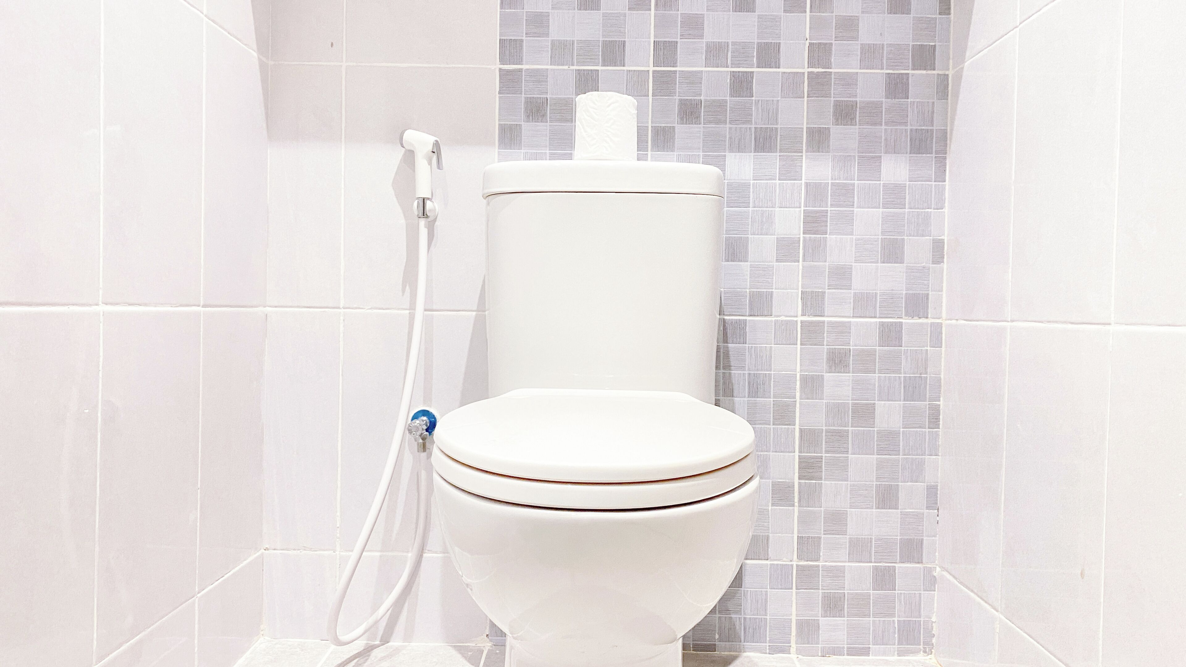 Een wit toilet met een bidetop in een badkamer met betegelde wanden.