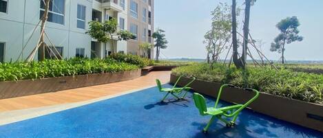 A rooftop terrace with a blue floor, green chairs, and a view of a building and trees.