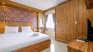 A hotel room with a large bed, wooden headboard, a wooden wardrobe, a TV, and a bedside table with a remote control.