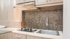 Eine moderne Küche mit Holzausstattung, einer Glasarbeitsplatte, einem Edelstahl-Spülbecken und einer strukturierten Spritzschutzwand.