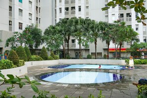 A swimming pool surrounded by palm trees and a building with balconies. - Comfort And Tidy 2Br At Green Bay Pluit Apartment Near Mall (Jakarta)