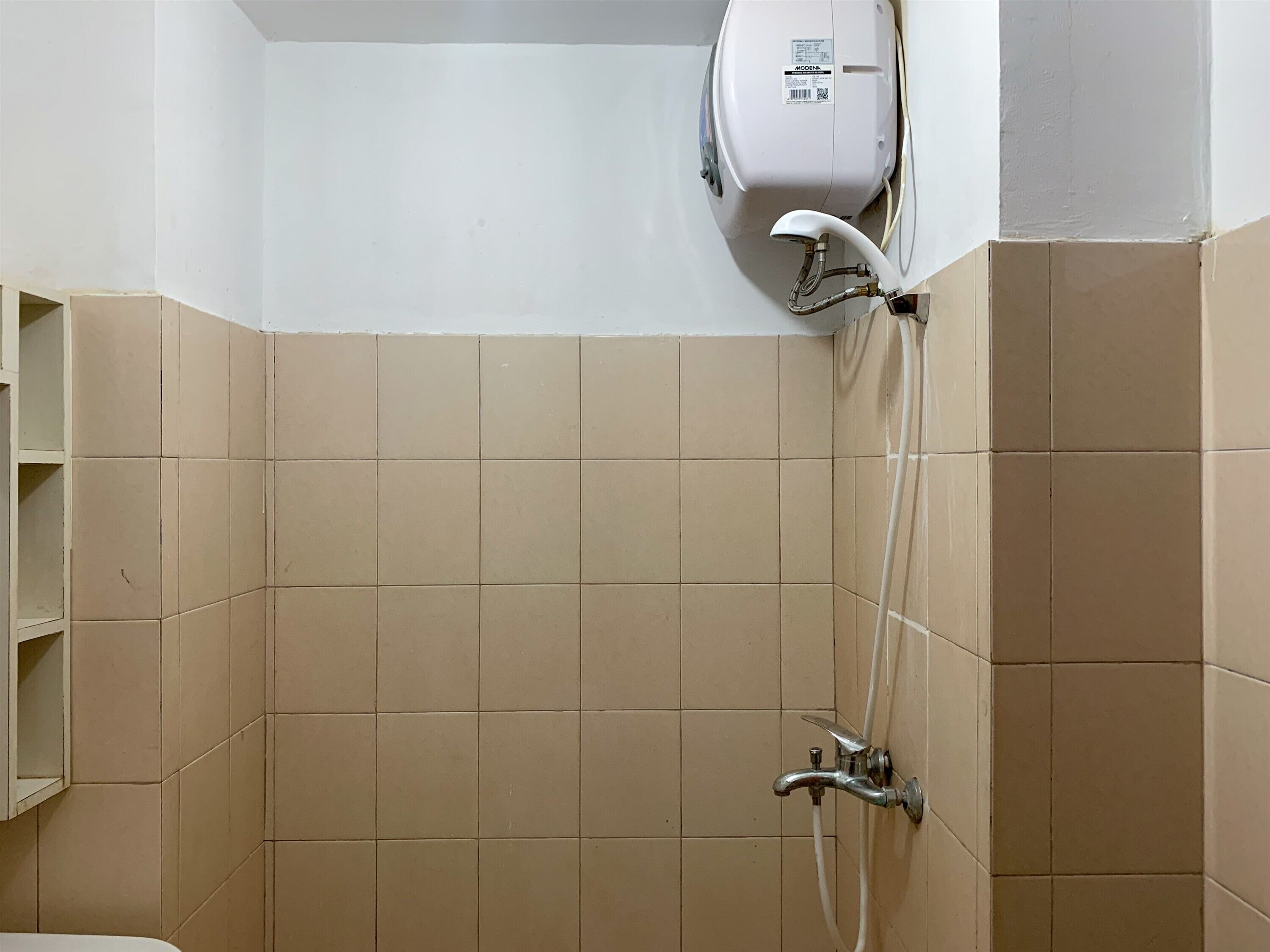A bathroom with beige tiles, a white toilet, and a wall-mounted shower unit.