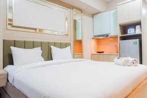Enjoy a comfortable stay in this stylish room featuring a neatly made bed, a large mirror, and a kitchenette with a microwave, kettle, and refrigerator.