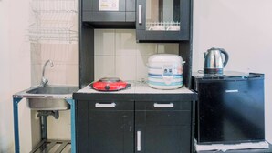 Une cuisine compacte équipée d’un évier, d’une plaque de cuisson à induction rouge, d’un grand cuiseur à riz et d’une machine à café noire.