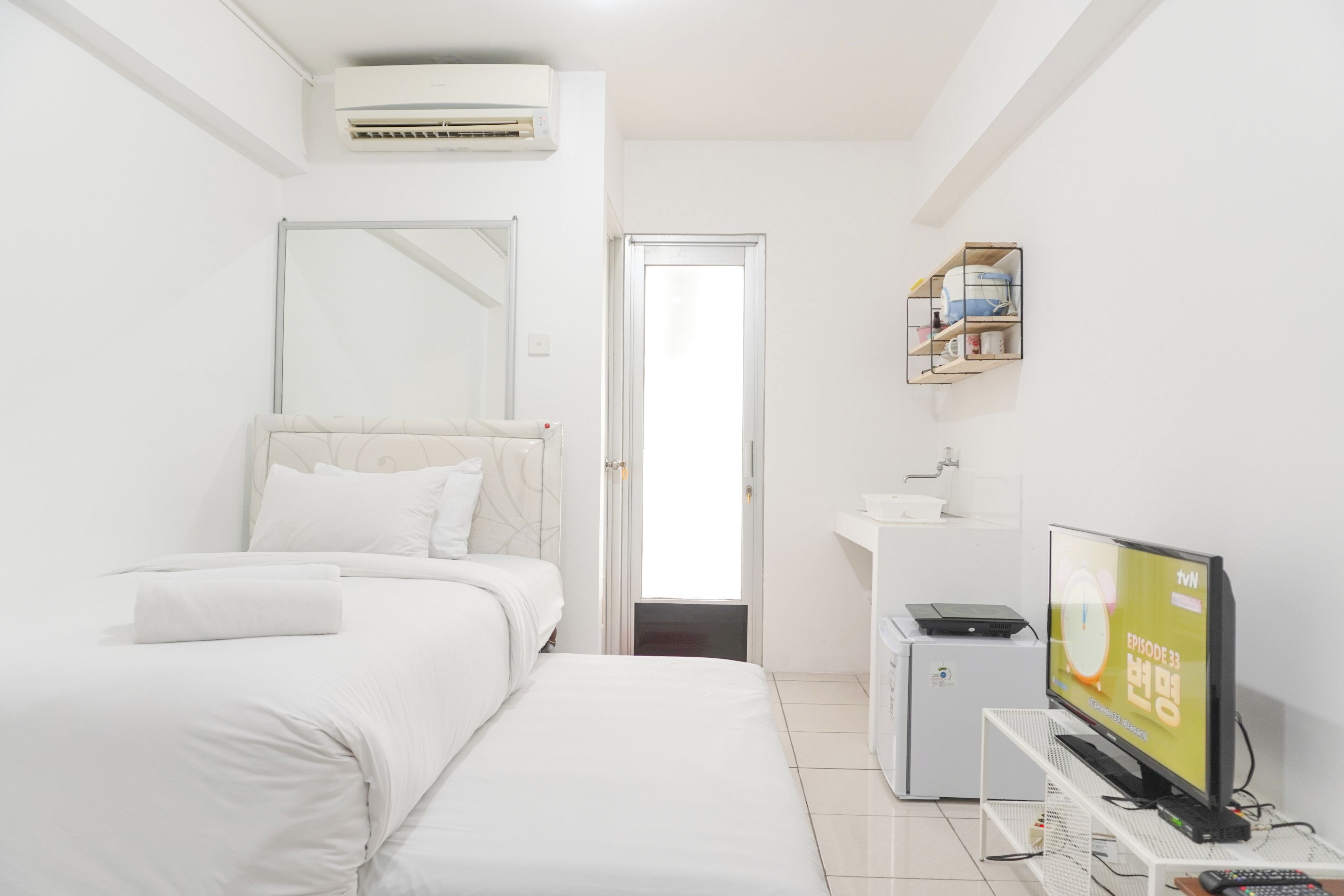Una camera d'albergo moderna con un letto, una scrivania, una televisione e un piccolo armadietto.